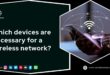 Hexagon-framed image with a black background. Left side: bold white text reads 'Which devices are necessary for a wireless network?' with a Techblonhub logo above and social media icons for Instagram, LinkedIn, Twitter, YouTube, Pinterest, Discord, Facebook, and WhatsApp below, followed by 'Follow Us:' in white. Right side: close-up of a person holding a smartphone with curved lines, dots, and a Wi-Fi icon, symbolizing a wireless network connection.